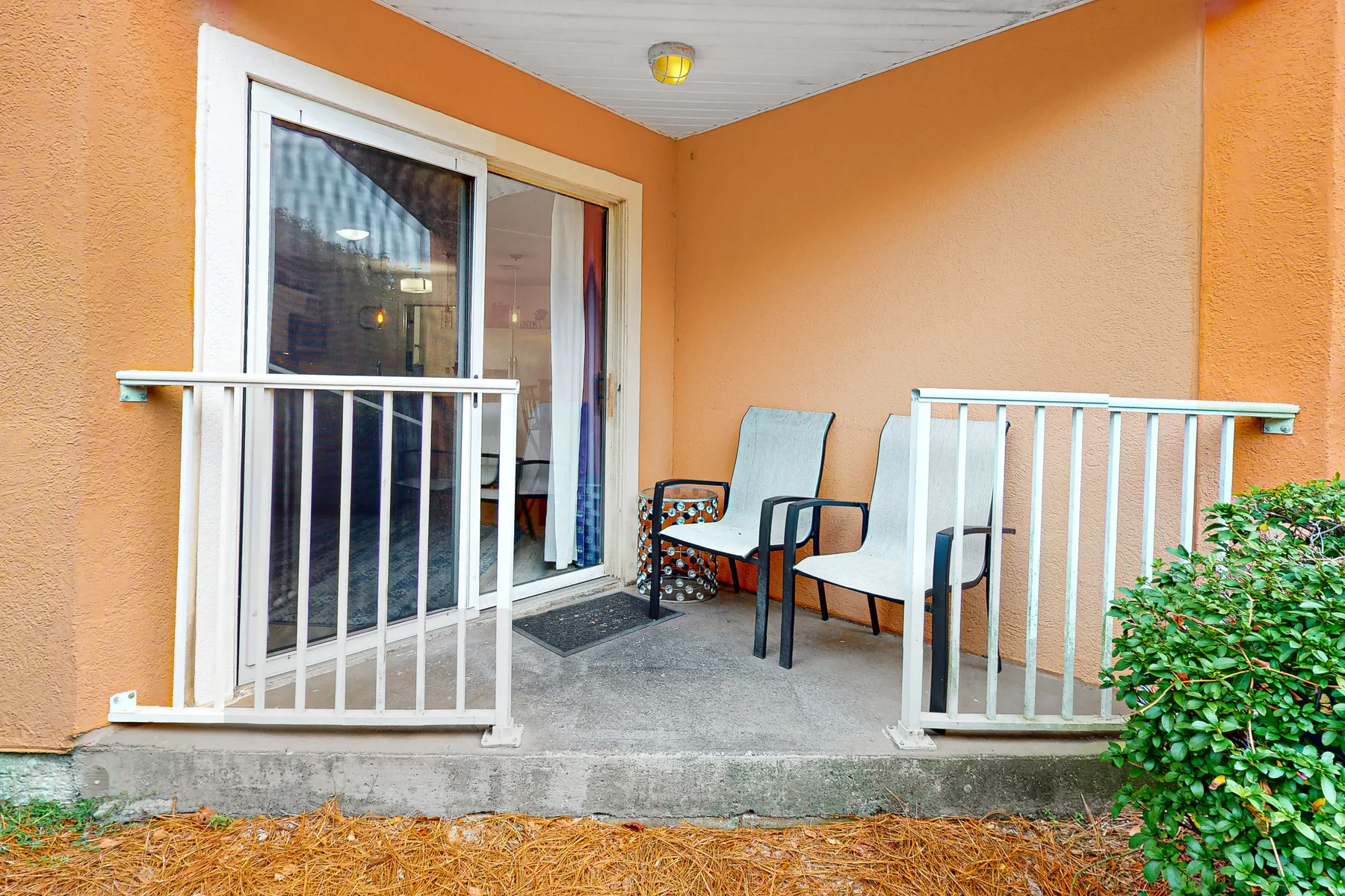 A covered patio has seating beside a sliding glass door.