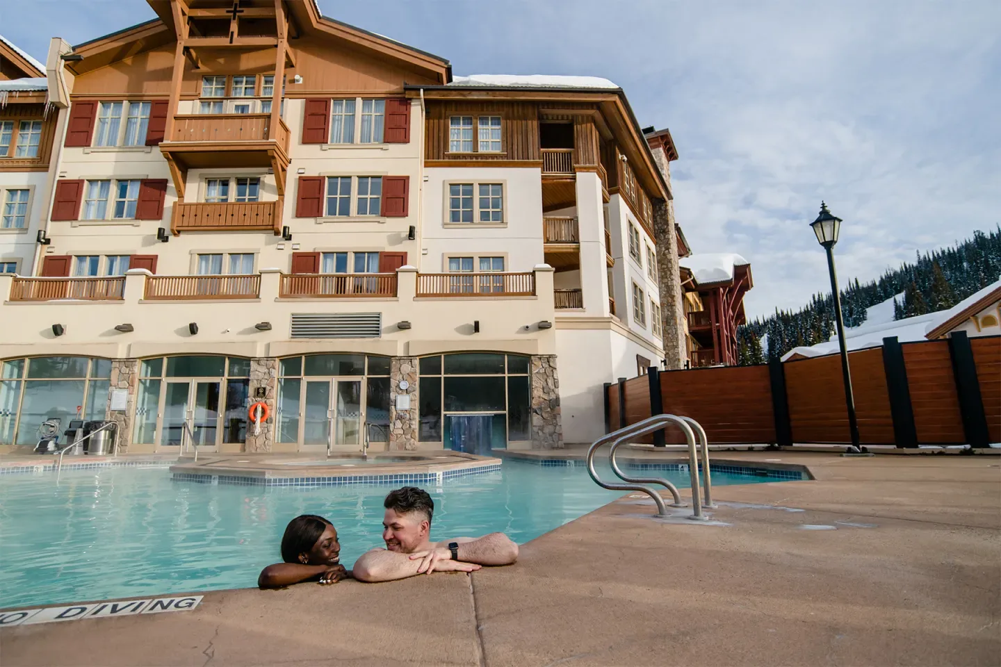 Guests relaxing in a pool beside the hotel and snowy mountains.