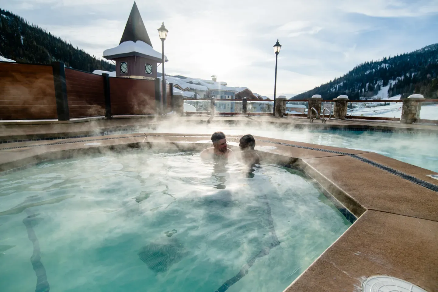 Guests relaxing in an outdoor pool beside snowy mountains.