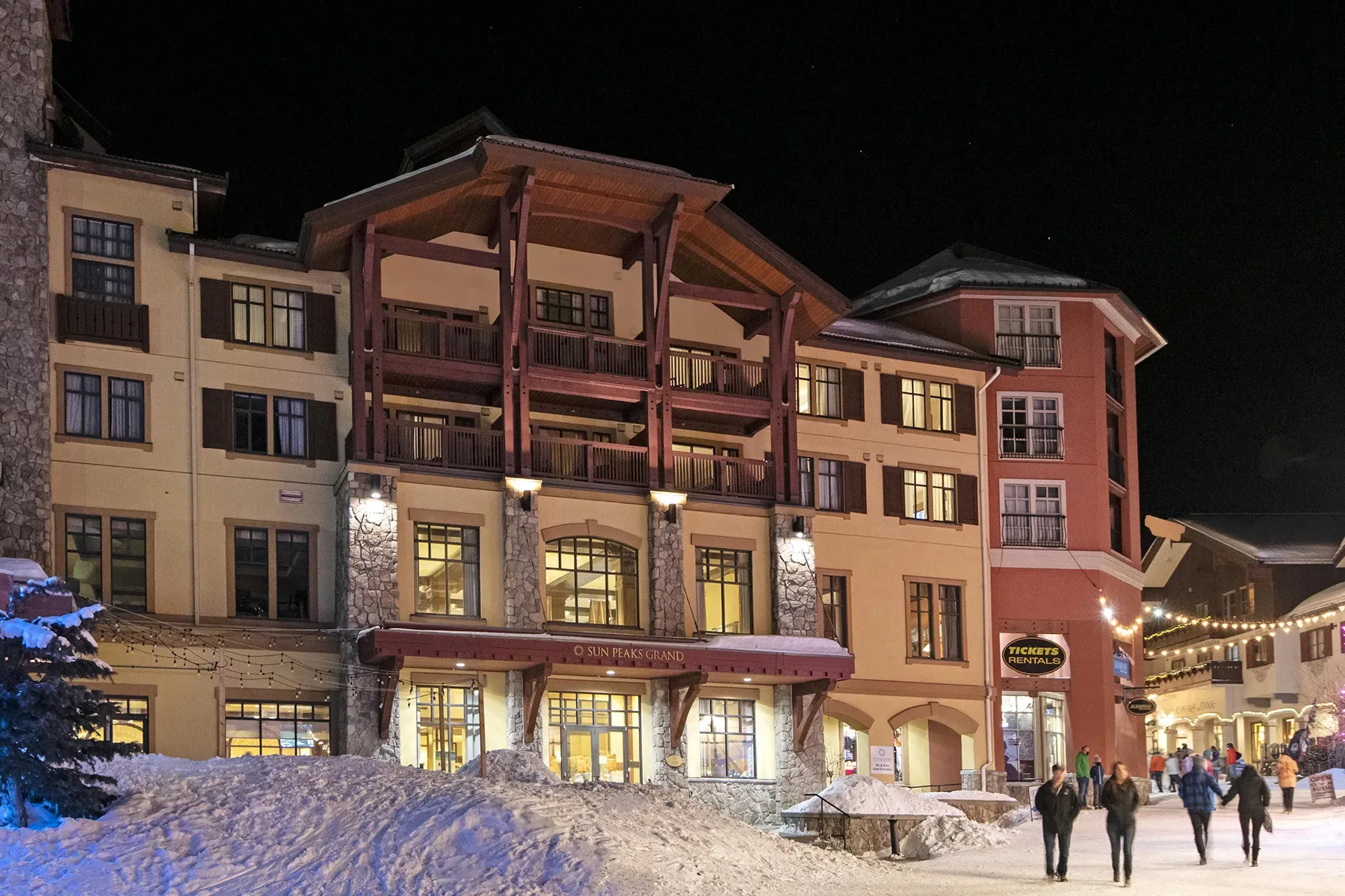 Edificios del complejo Sun Peaks Grand con iluminación cálida por la noche, rodeados de nieve.
