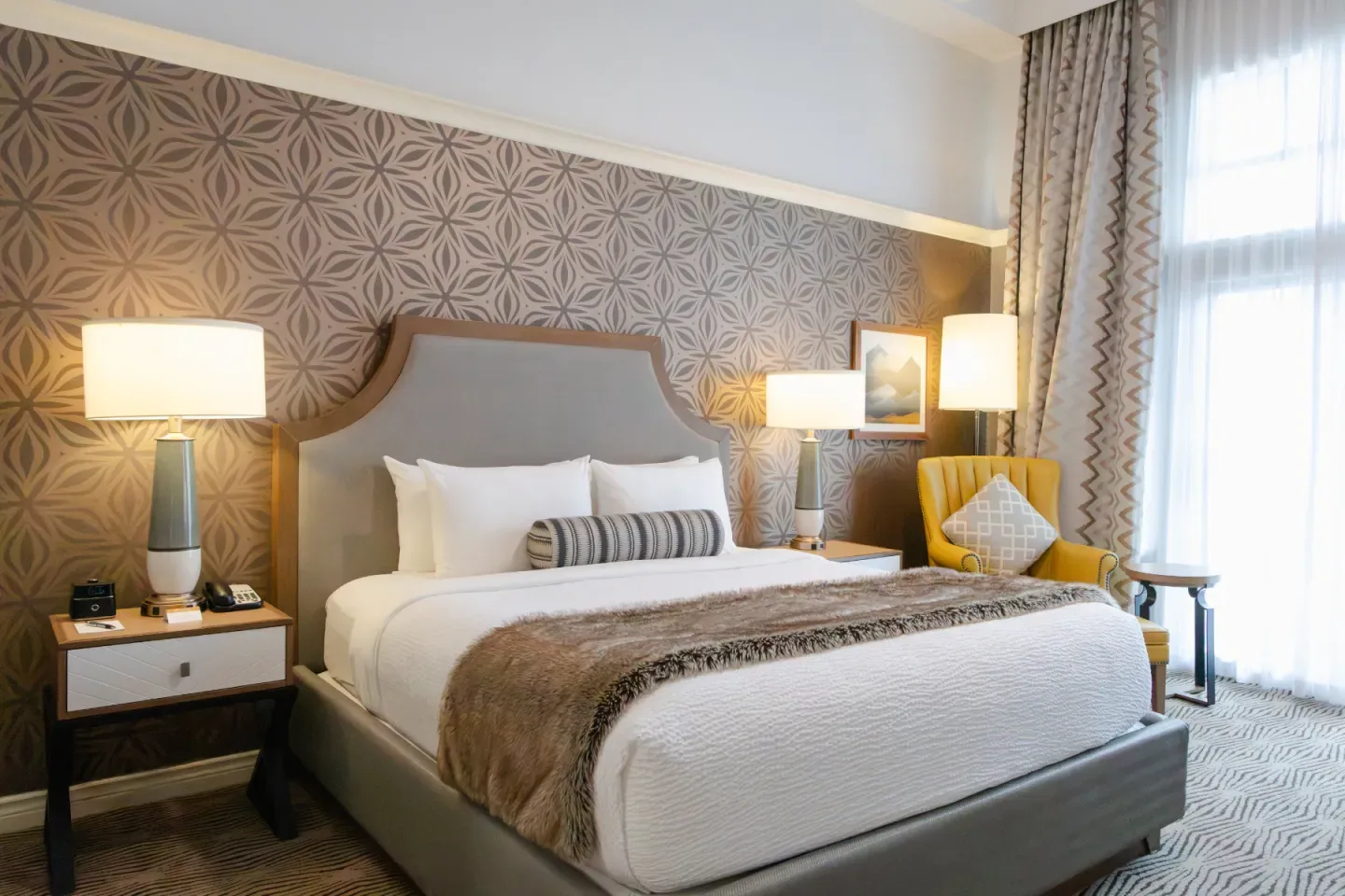 Habitación de hotel con una cama grande, papel tapiz estampado y lámparas de noche.