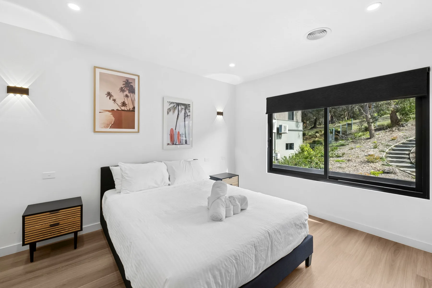 Un dormitorio luminoso con ropa de cama blanca y una ventana amplia con vistas a la vegetación.