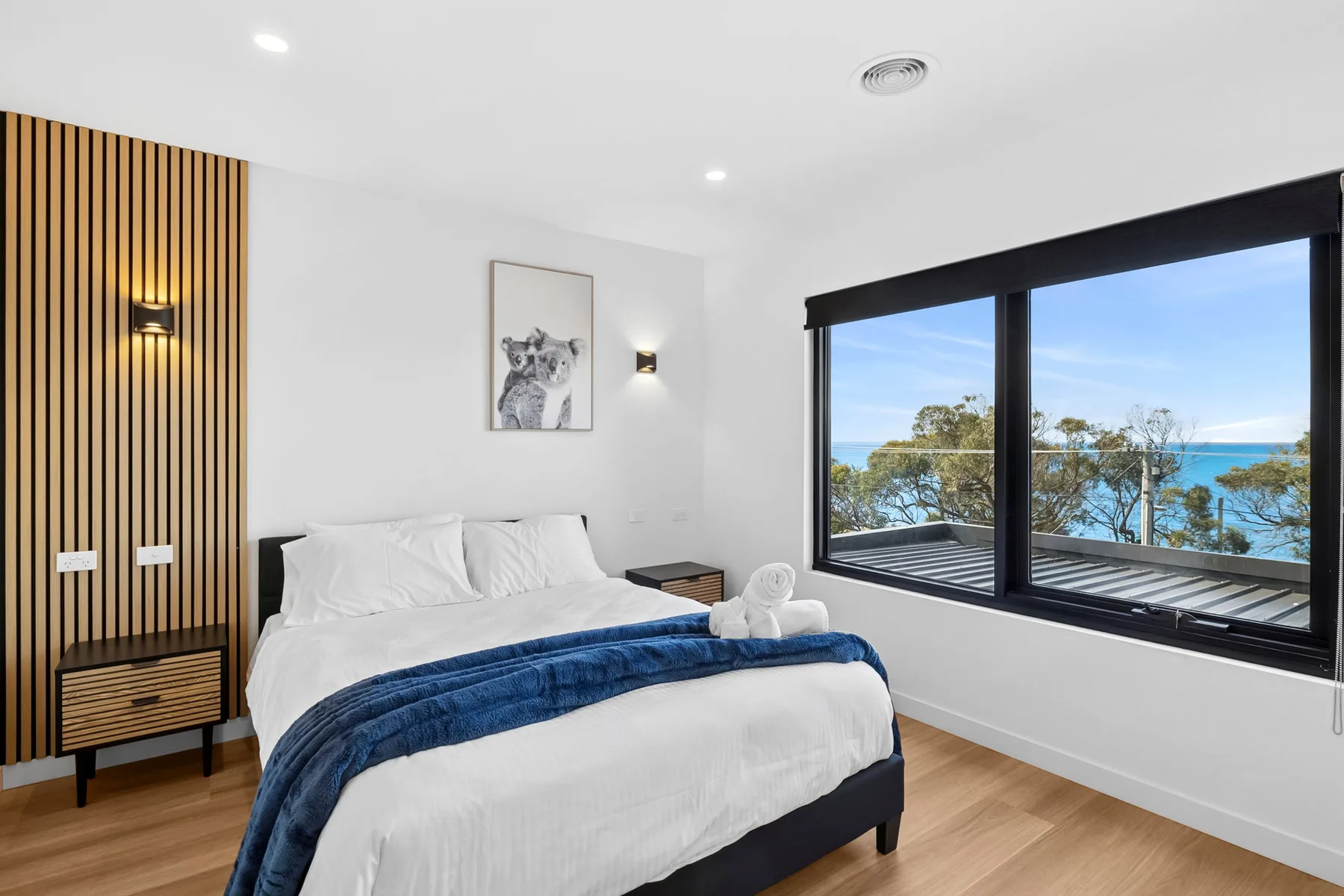 Dormitorio con ropa de cama blanca y una gran ventana con vistas al agua.