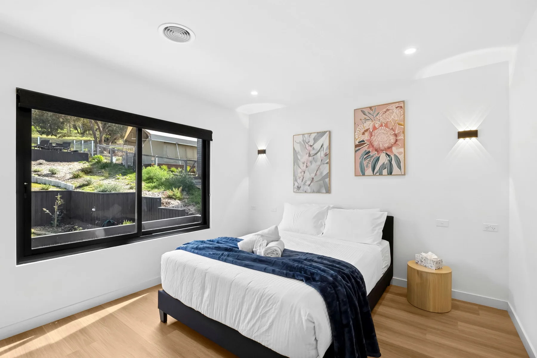 Un dormitorio luminoso con una cama bajo dos cuadros florales.