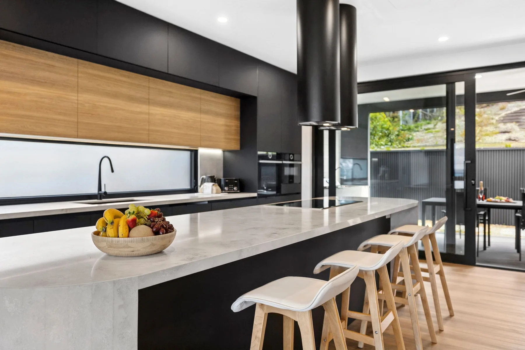 Una cocina moderna con una isla larga y taburetes junto a grandes puertas de vidrio.