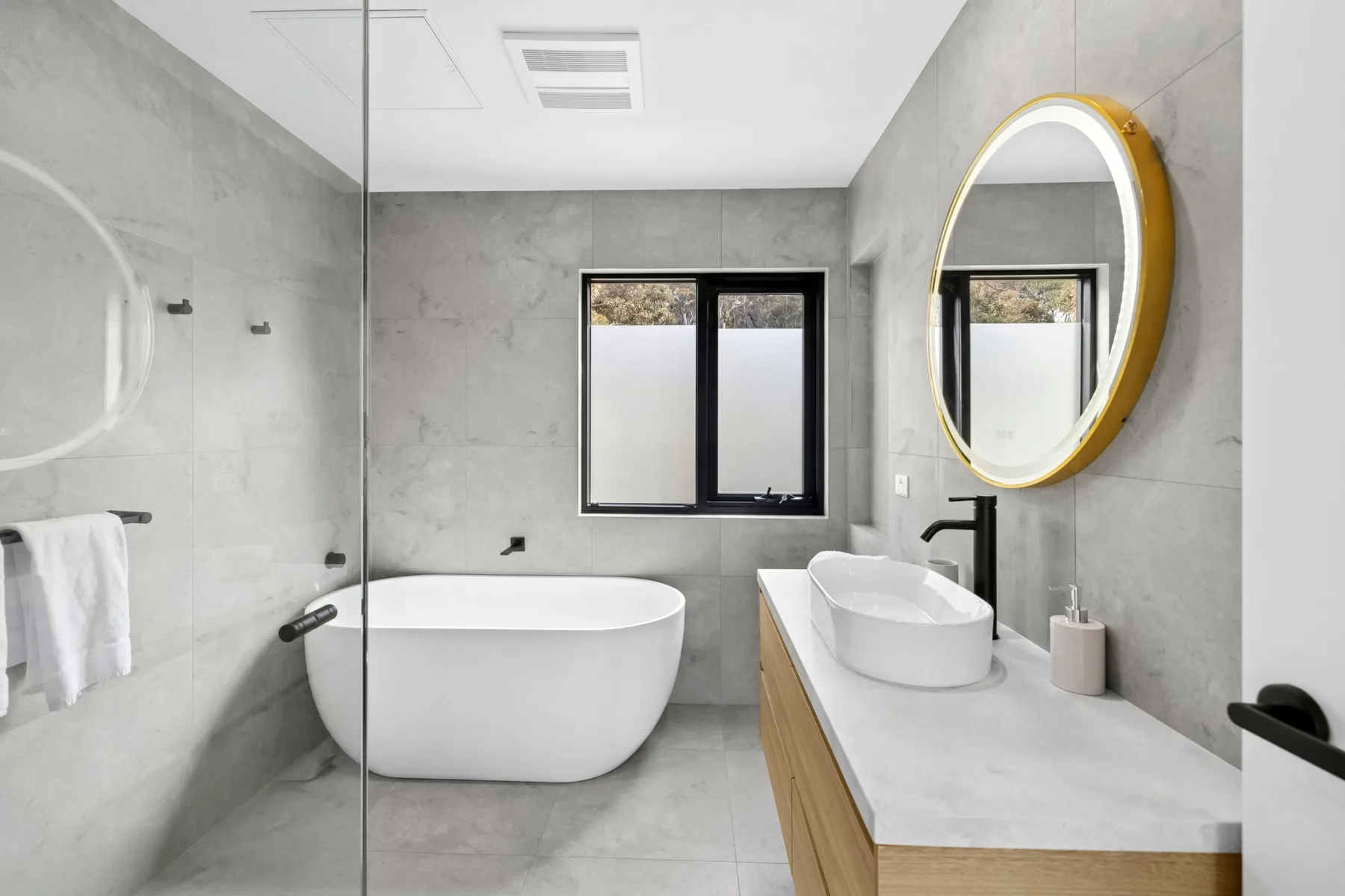 Un baño moderno con bañera, lavabo sobre encimera y espejo redondo.