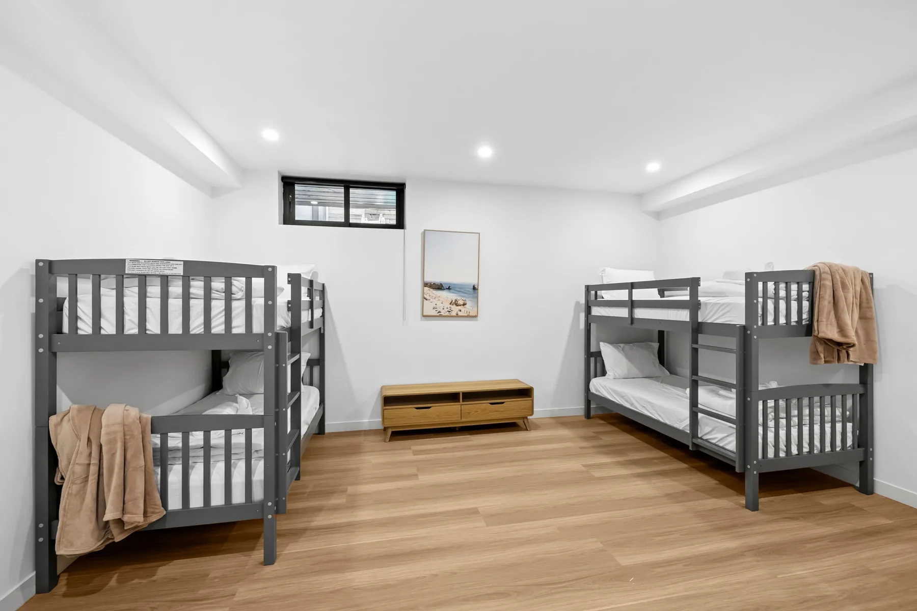 Un dormitorio con literas, suelo de madera y un mueble bajo.