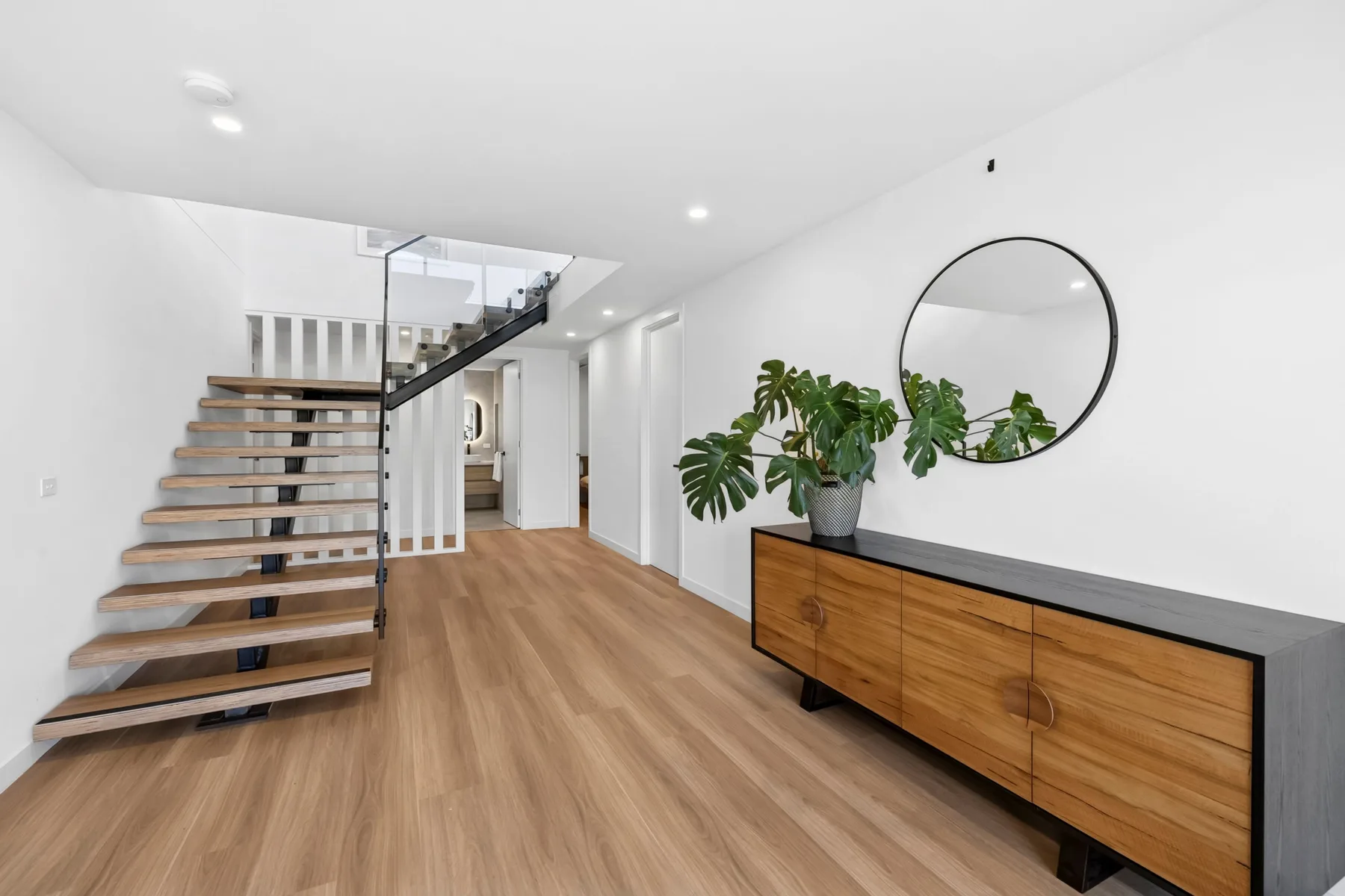 Un pasillo interior luminoso con una escalera y suelo de madera.