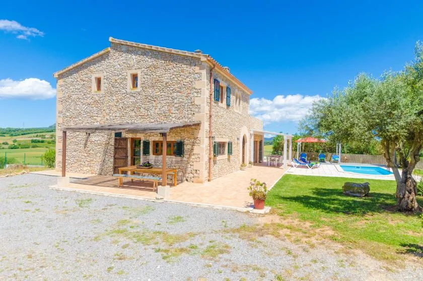 A stone house with a covered patio beside a swimming pool and garden.