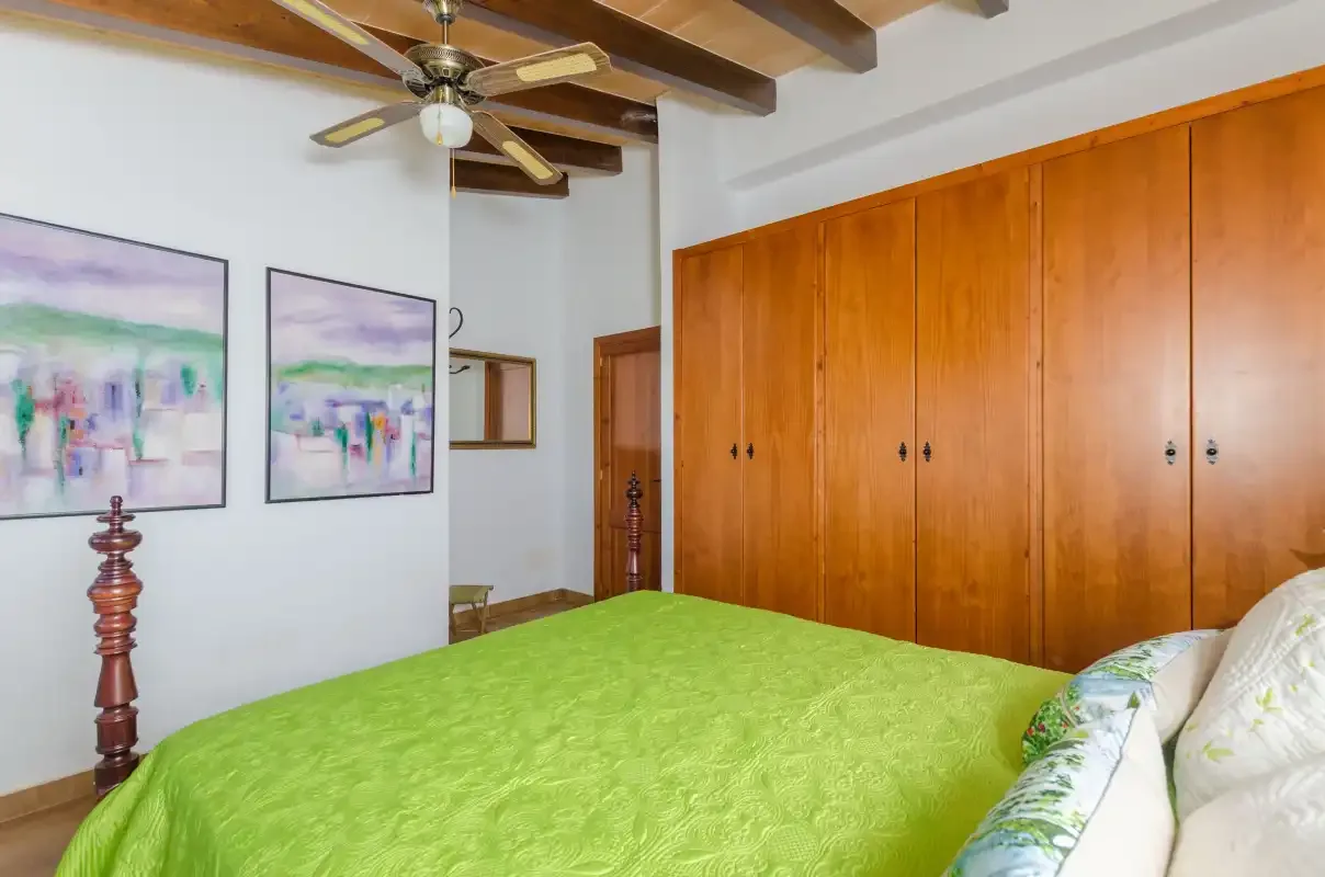 A bedroom with a green bedspread, wooden wardrobes, and framed wall art.