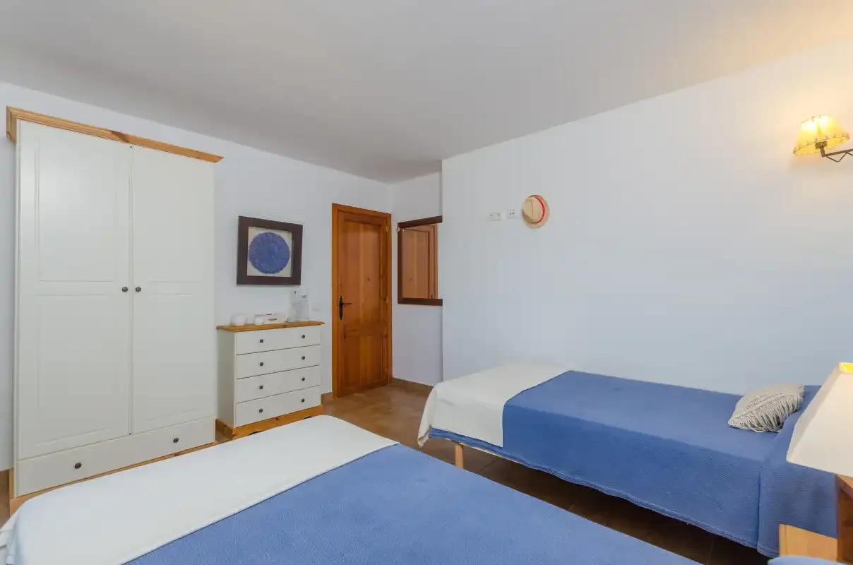 A bedroom with blue bedding, a wardrobe, and a chest of drawers.