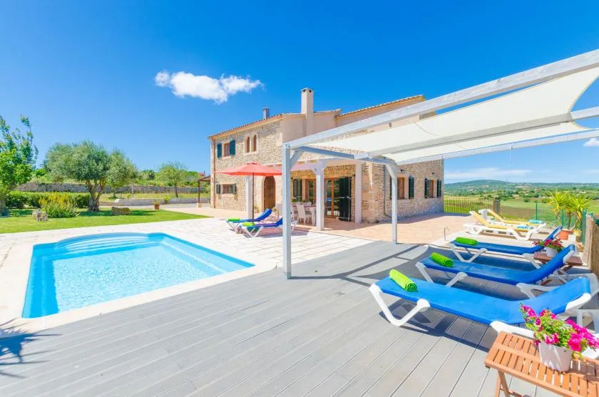 Una piscina al aire libre y un patio soleado junto a una casa de piedra.