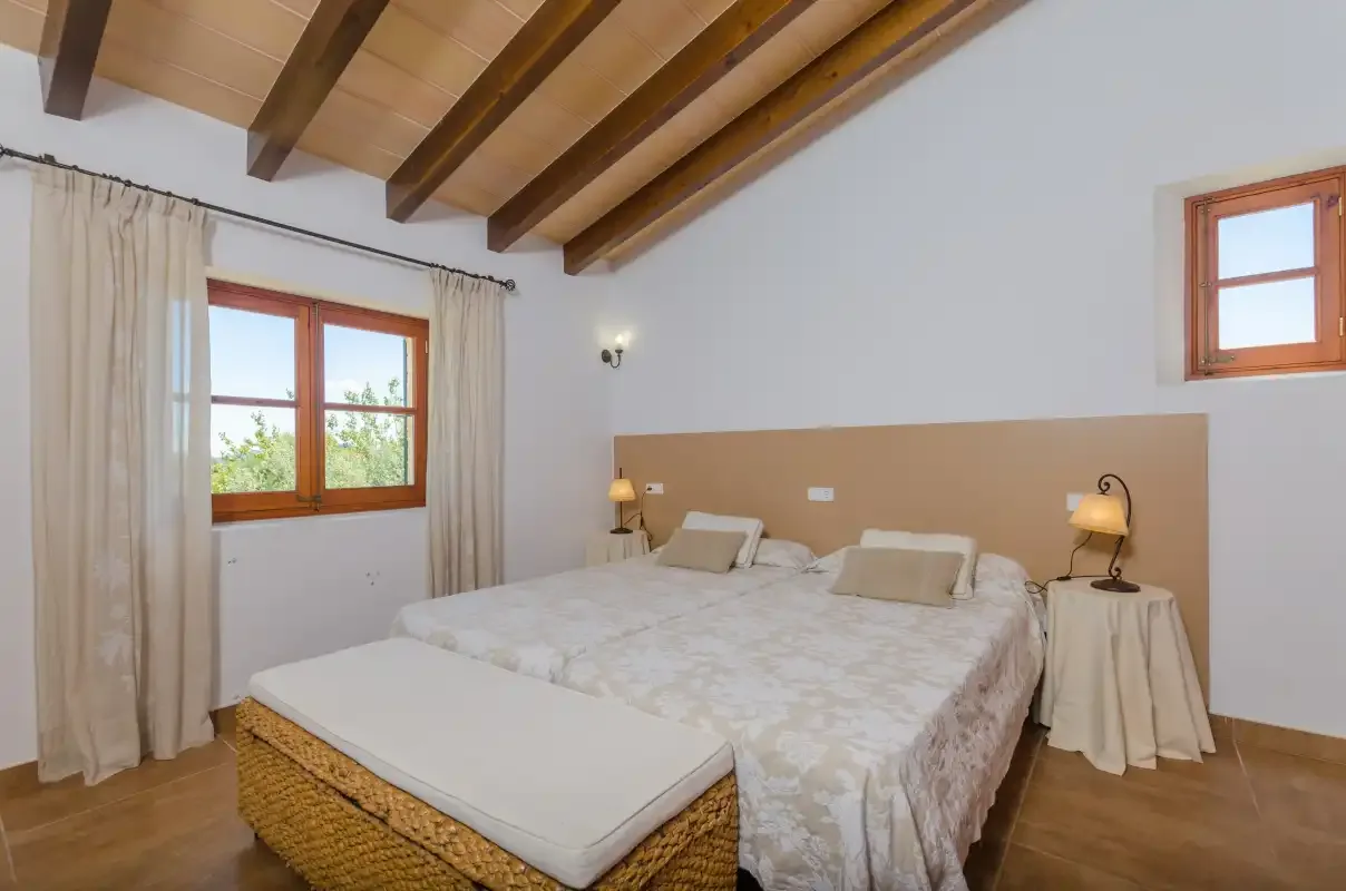 A bedroom with a large bed, bedside tables, and exposed wooden ceiling beams.