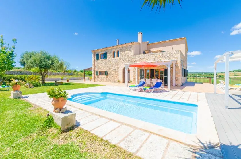 A stone house stands beside a swimming pool and patio.