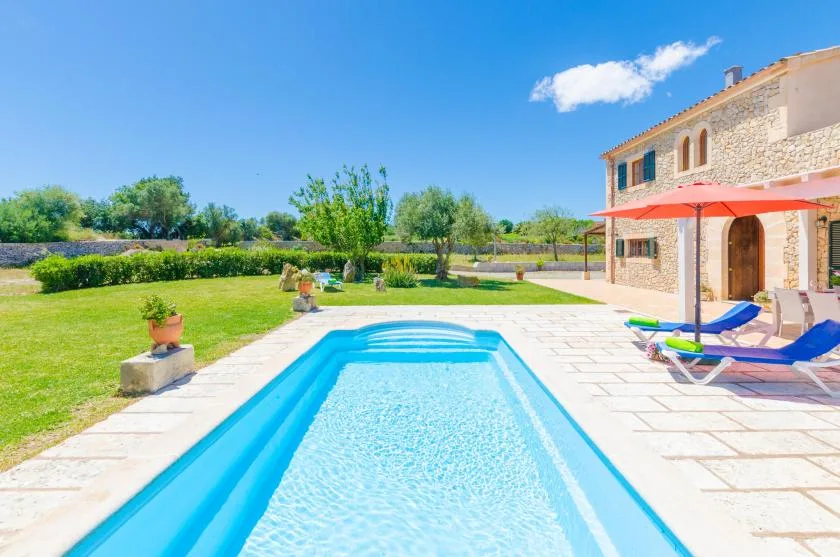 An outdoor swimming pool beside a stone house and sunny patio.