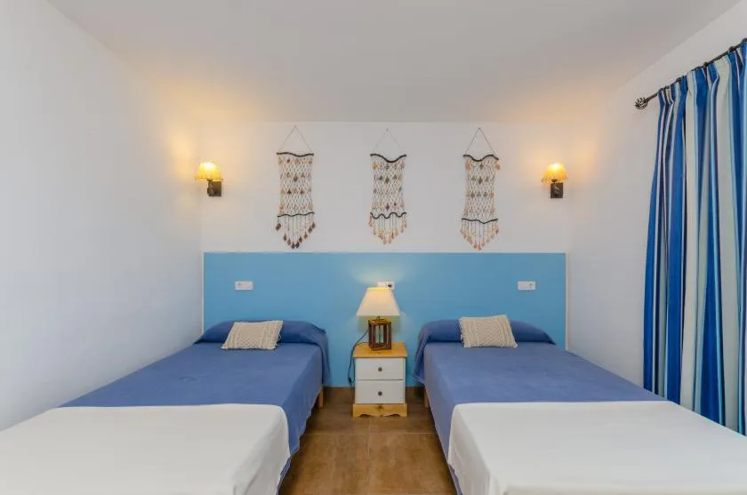 A bedroom with two beds, blue bedding, and a small nightstand between them.