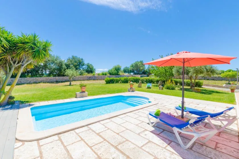An outdoor swimming pool sits beside a paved patio and red umbrella.