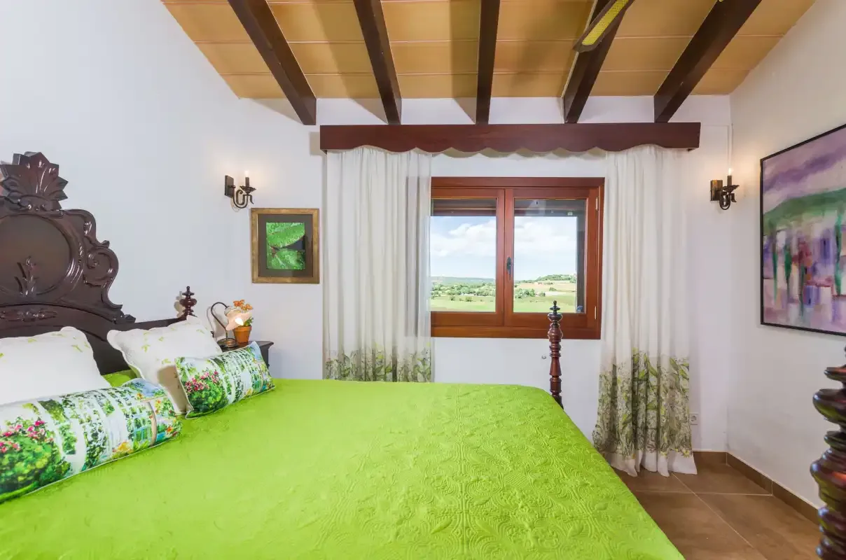 A bedroom with a green bedspread and a window overlooking the countryside.