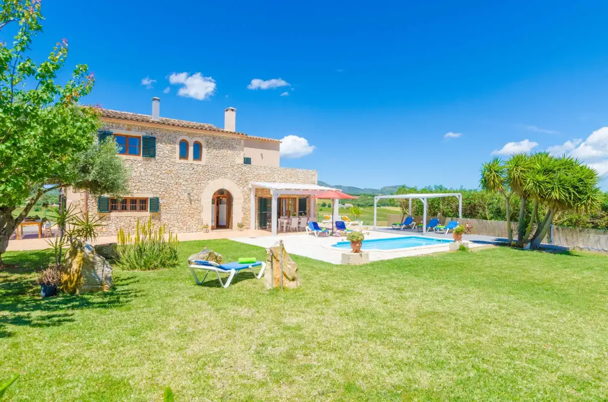 A stone house opens onto a grassy garden with a swimming pool.