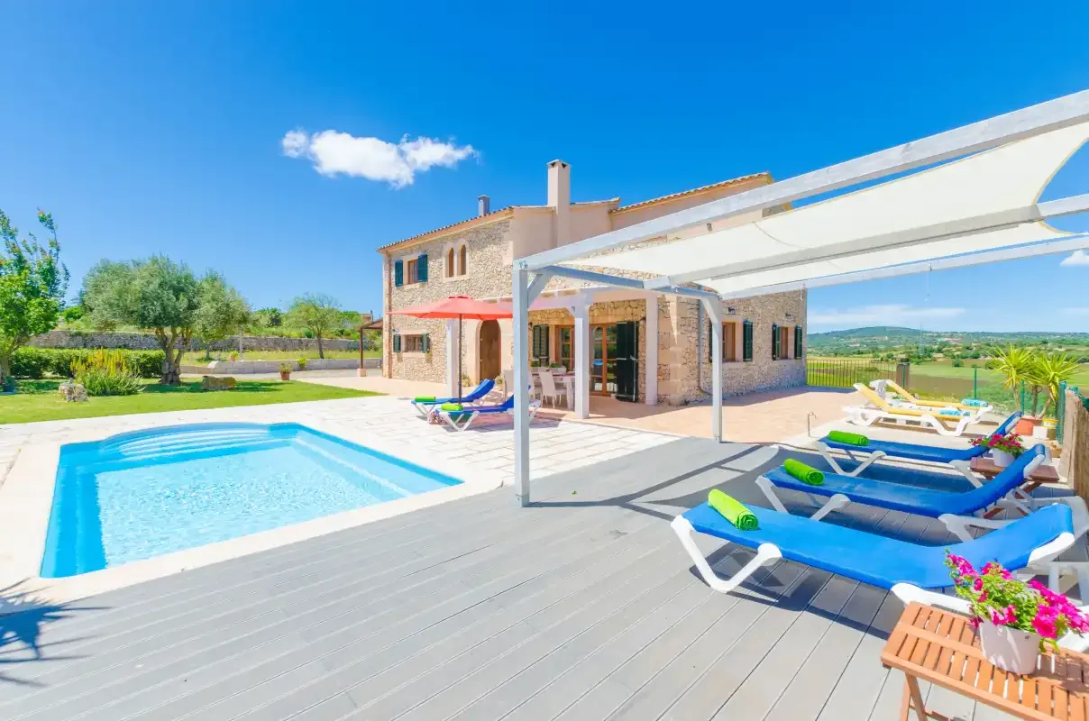A swimming pool and sun loungers sit beside a house on a sunny patio.