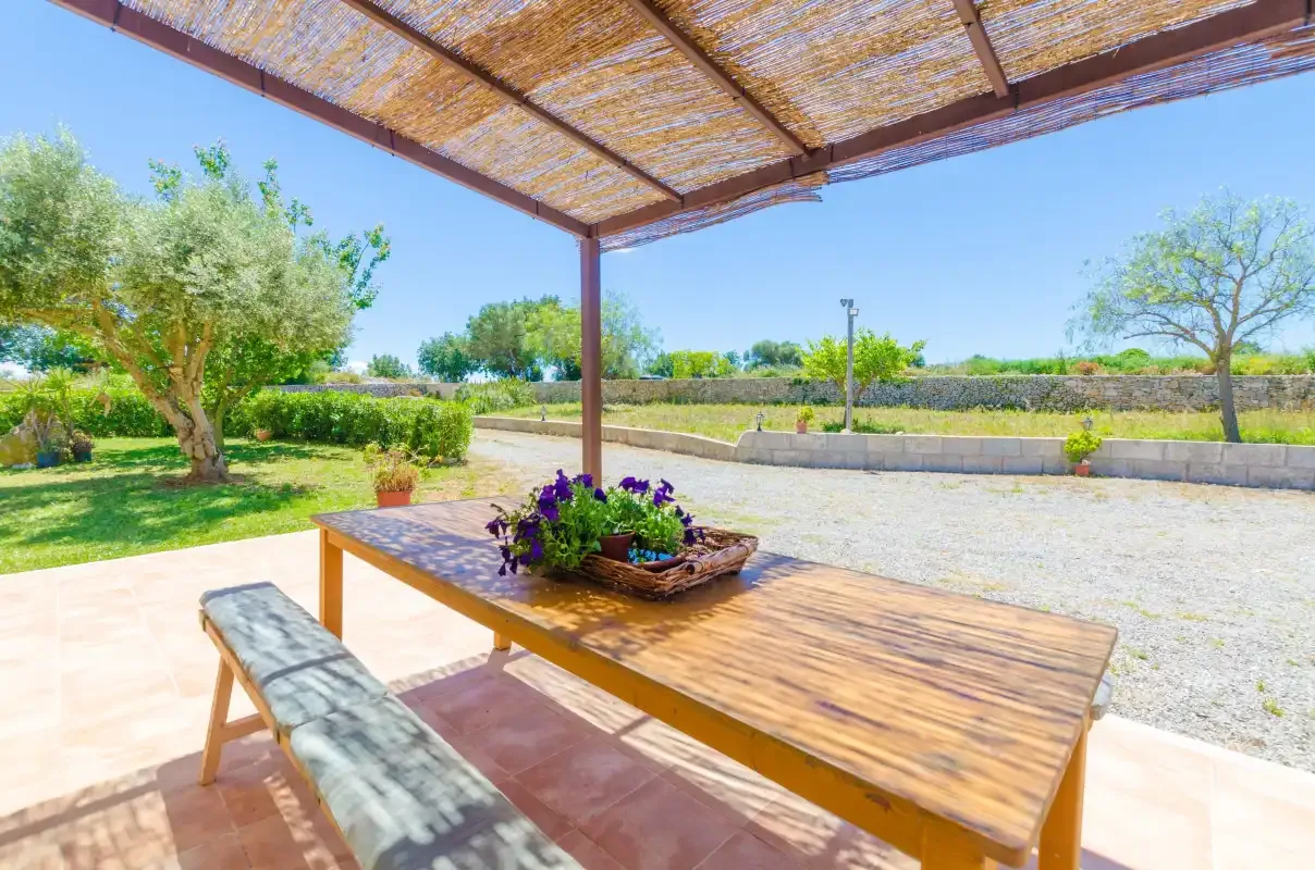 A shaded outdoor dining area overlooks a garden and open fields.