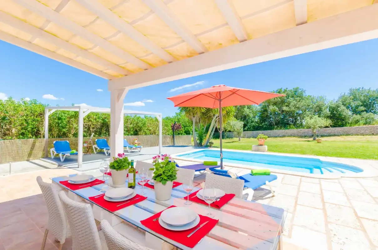 A shaded outdoor dining area overlooks a swimming pool and garden.