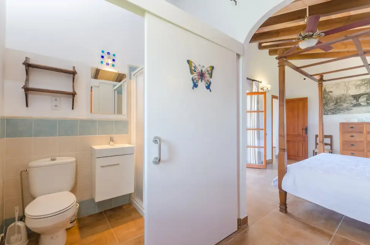 A bedroom with an adjoining bathroom and a white bed.
