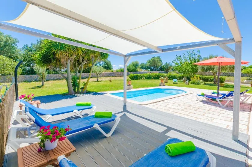 A swimming pool beside a shaded deck with lounge seating and greenery.