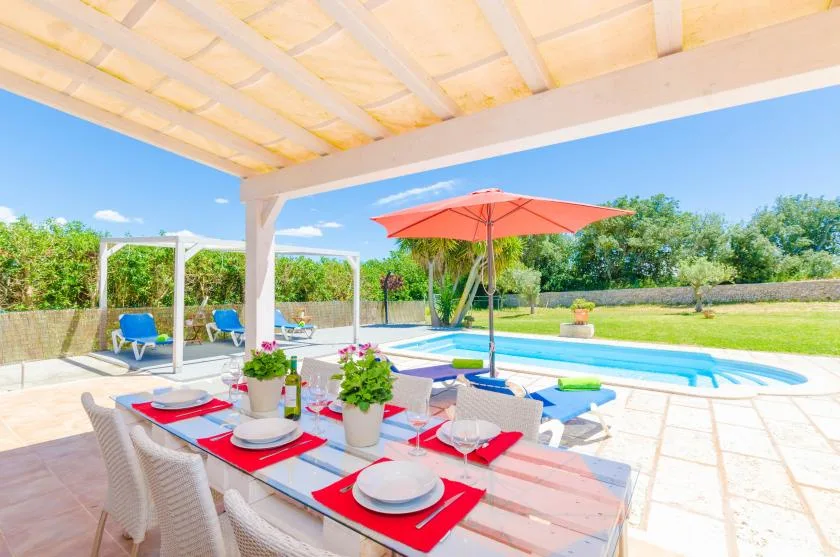 Una zona de comedor cubierta da a una piscina y un jardín.