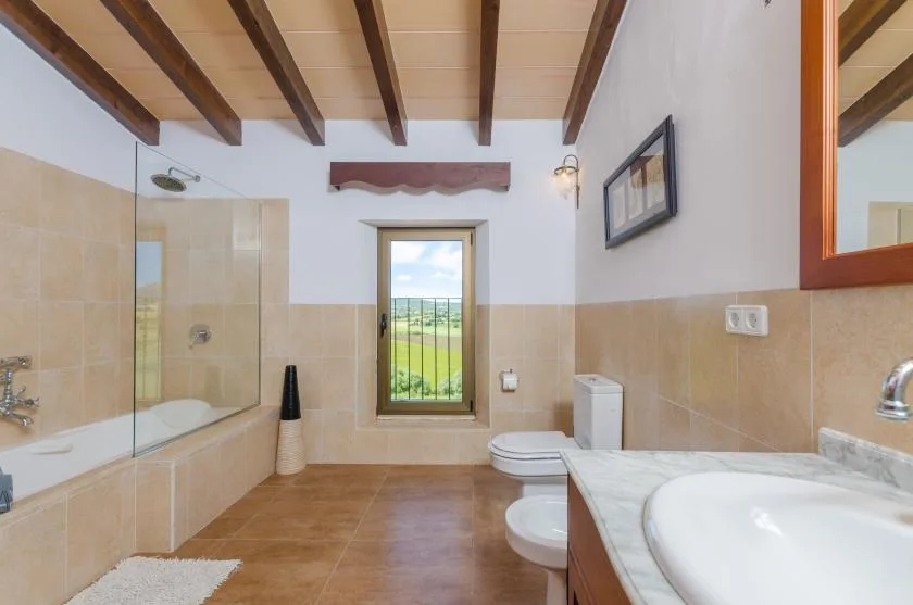 A bathroom with a bathtub, shower, sink, and a window overlooking green fields.