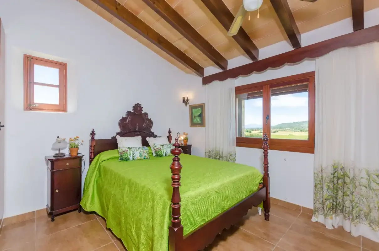 A bedroom with a green-covered bed beneath exposed wooden ceiling beams.