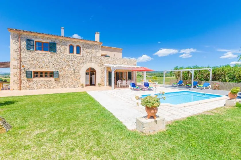 A stone house overlooks a swimming pool, patio, and green lawn.