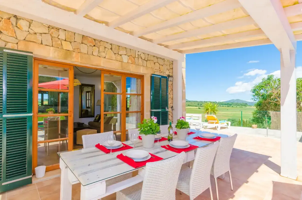 A covered outdoor dining area with a set table overlooking open countryside.