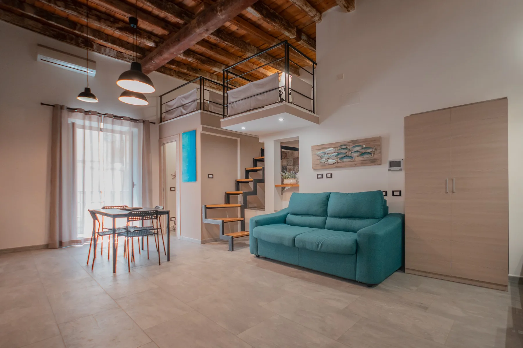 A living area with teal seating, a dining table, and a raised sleeping loft.