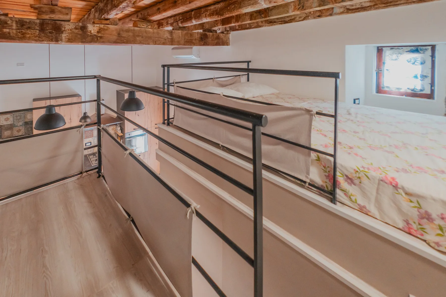 A loft bedroom with bunk beds beneath exposed wooden ceiling beams.