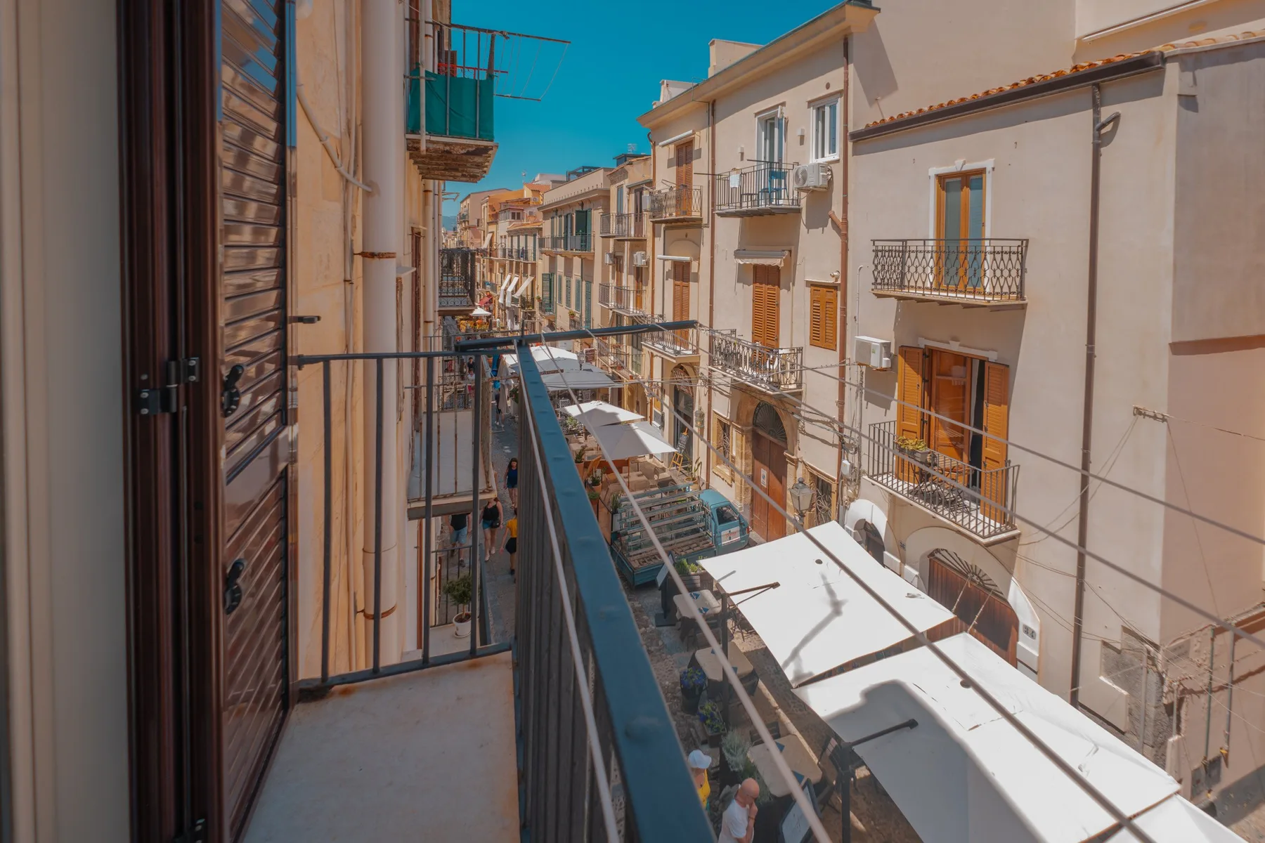 A balcony overlooks a narrow street lined with buildings and café awnings.