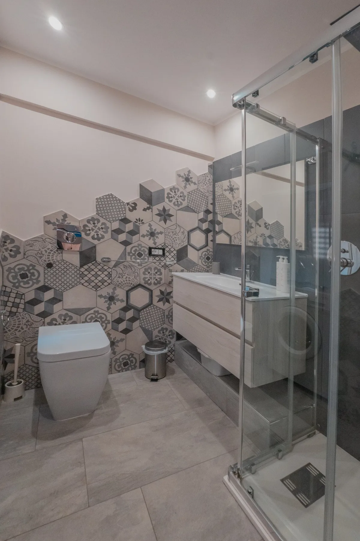 A modern bathroom with patterned wall tiles and a glass shower.