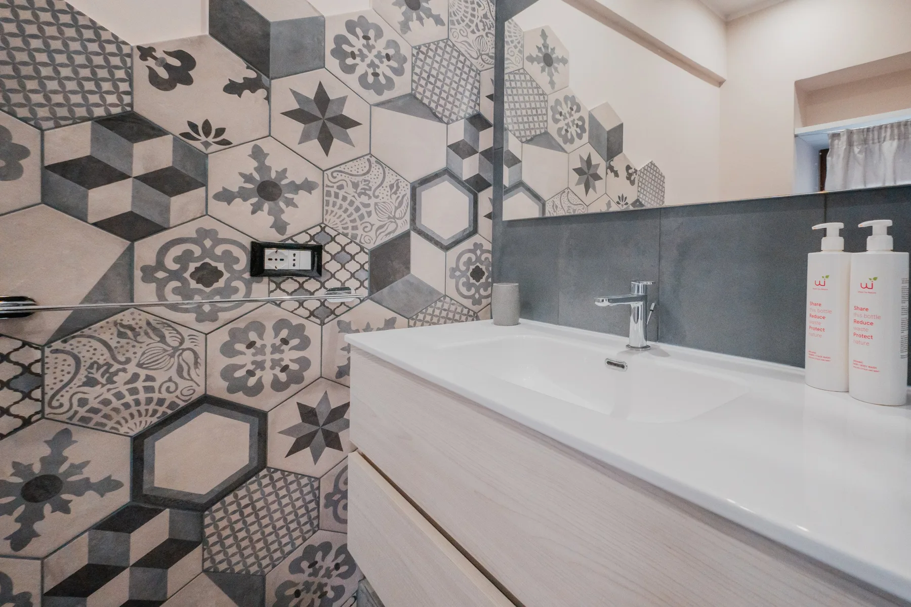 A bathroom vanity with a sink sits beside a wall of patterned tiles.