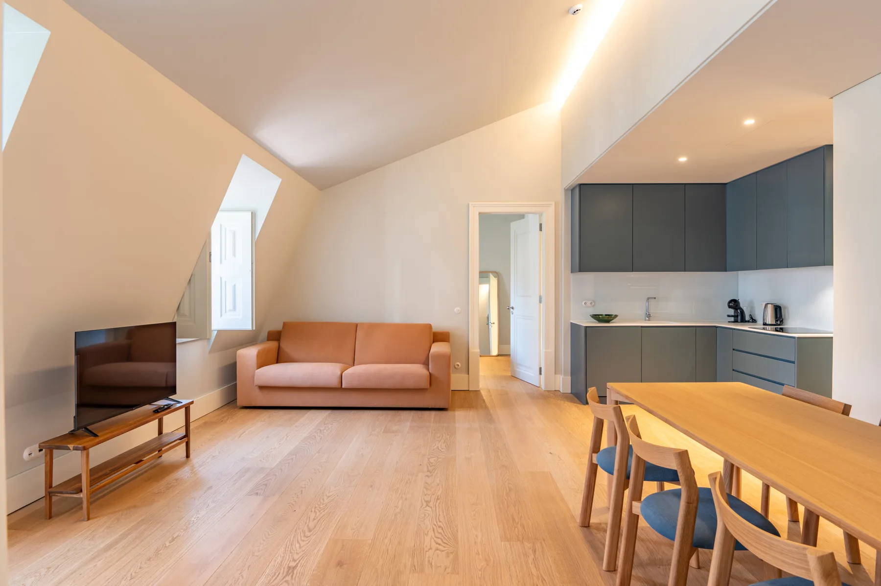 Una luminosa sala de estar y comedor diáfana con sofá, televisor y cocina.