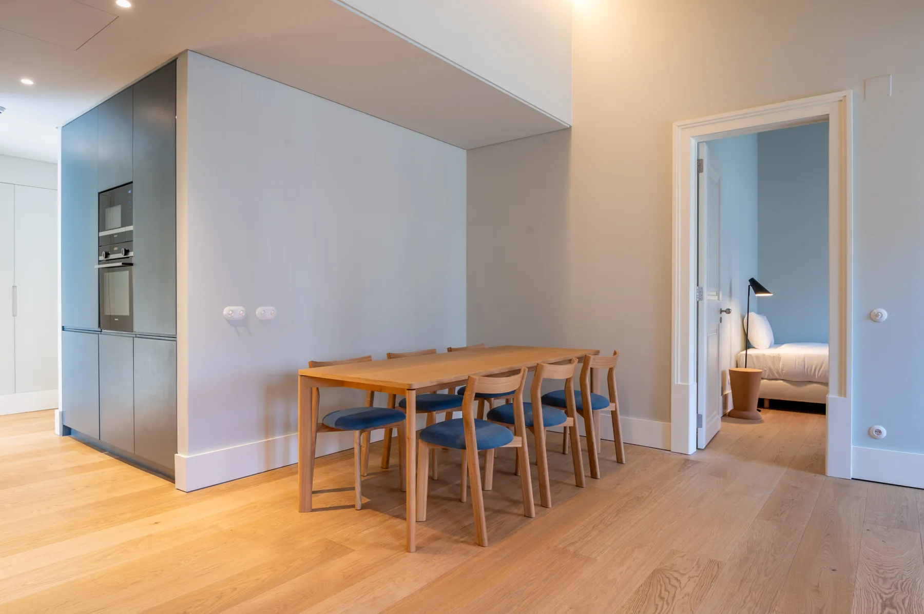 Comedor con una mesa de madera y sillas junto a la puerta abierta de un dormitorio.