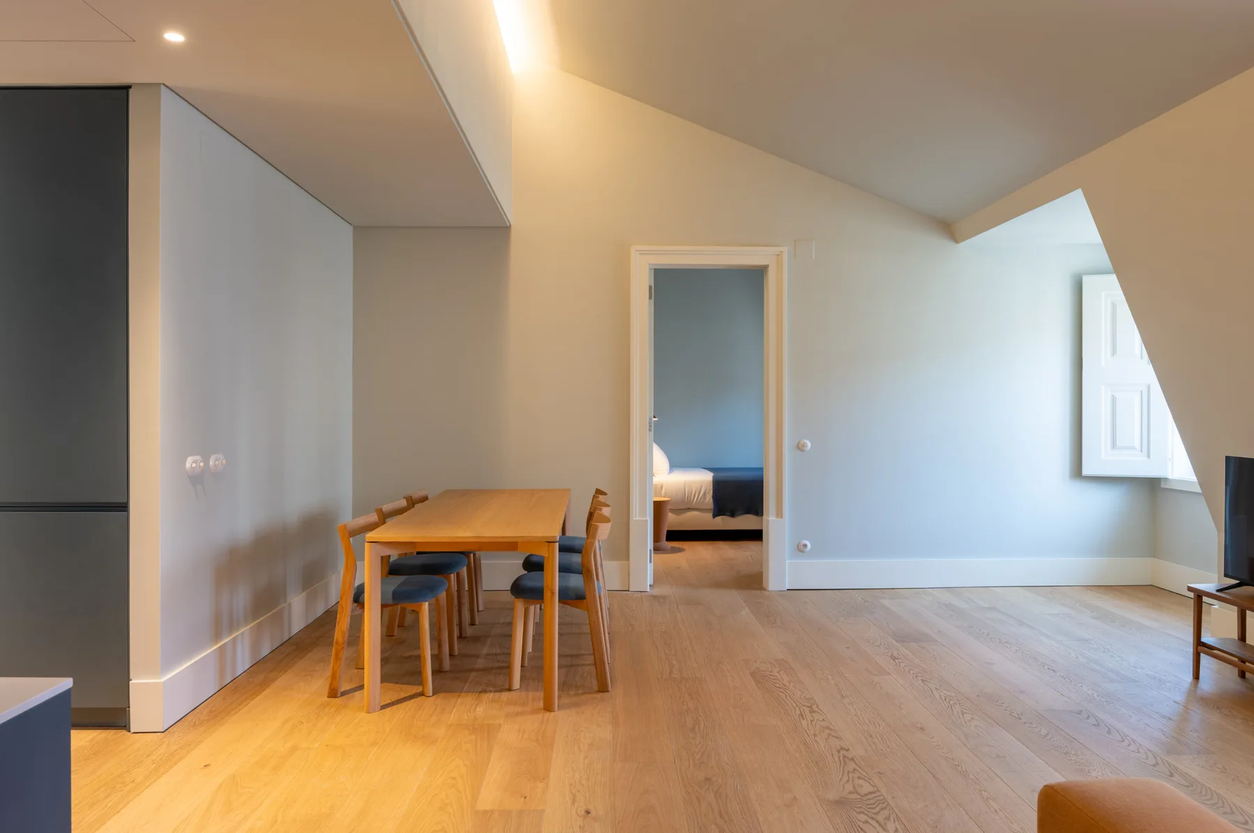 Comedor abierto con mesa y sillas de madera junto a la entrada de un dormitorio.