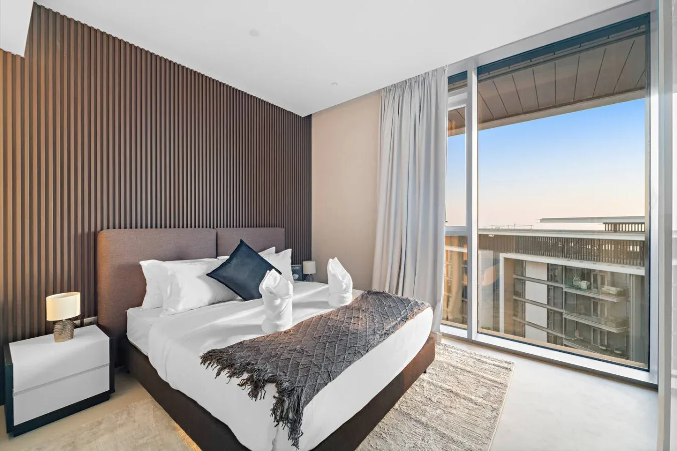 Un dormitorio con una cama tendida junto a grandes ventanas y cortinas.