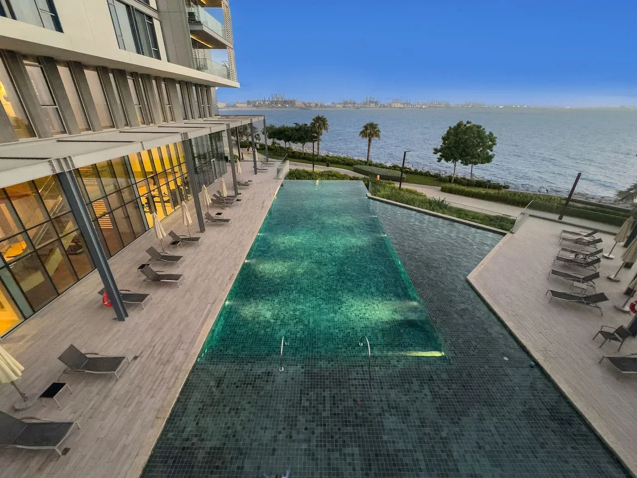 Una piscina al aire libre junto a un edificio frente al agua, con asientos en la terraza.