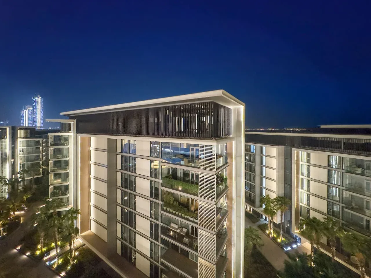 Un edificio residencial moderno está iluminado por la noche bajo un cielo azul oscuro.