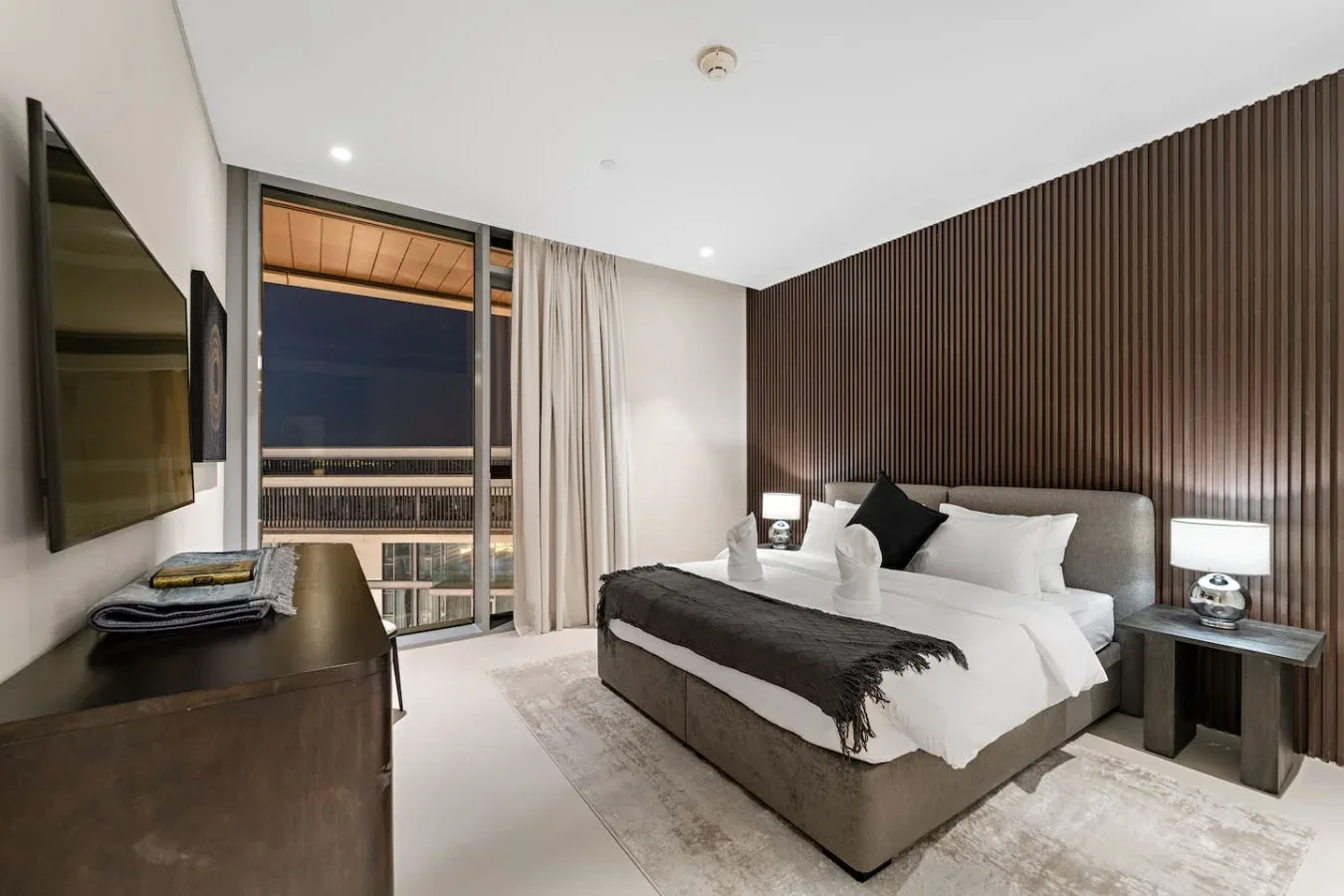 Un dormitorio con una cama bien tendida junto a una ventana grande.