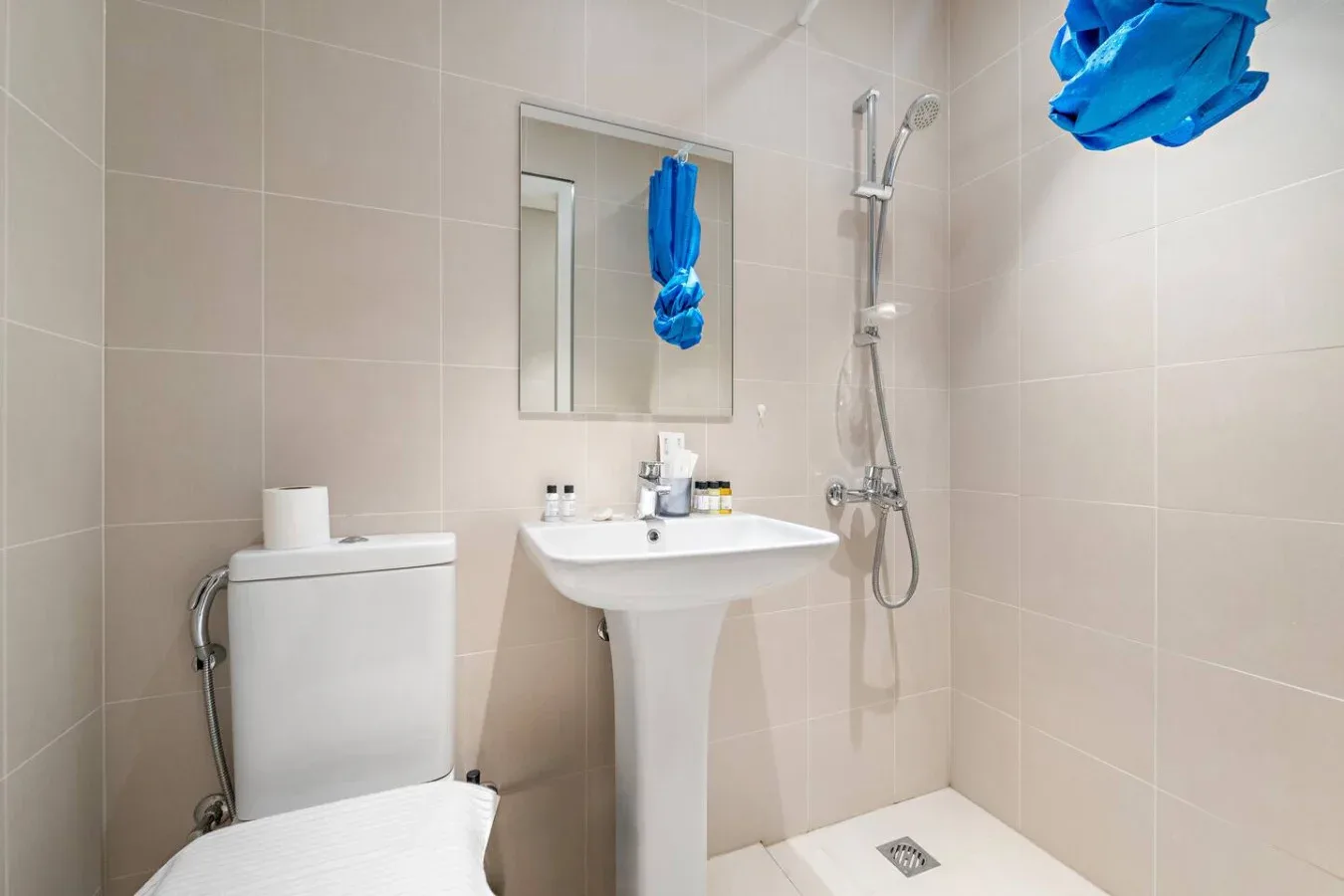 Un baño alicatado con inodoro, lavabo con pedestal y ducha de pared.