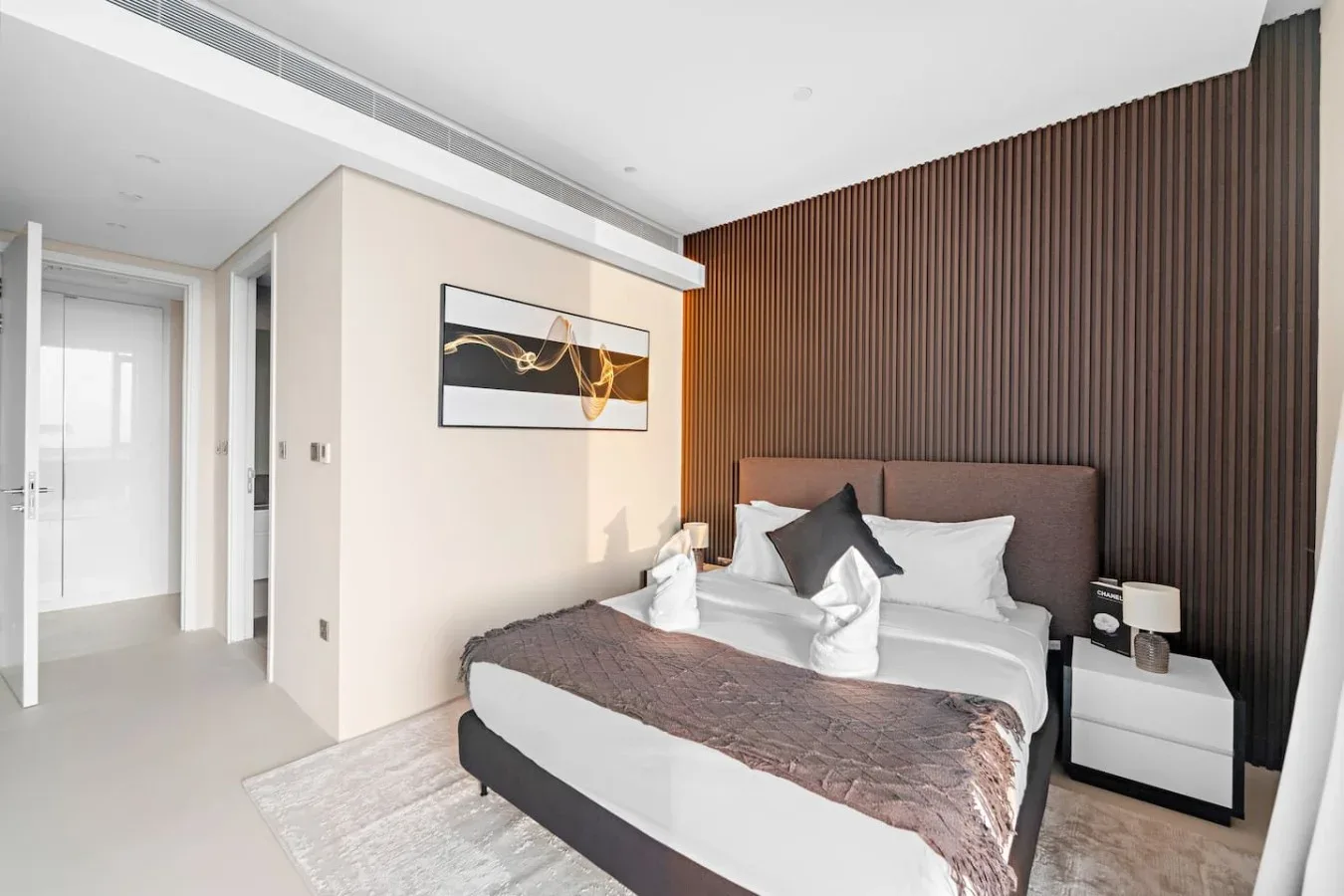 Un dormitorio con una cama bien arreglada junto a una pared oscura con paneles.