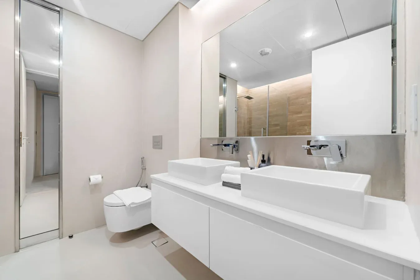 Un baño moderno y luminoso con dos lavabos y un inodoro junto a un espejo grande.