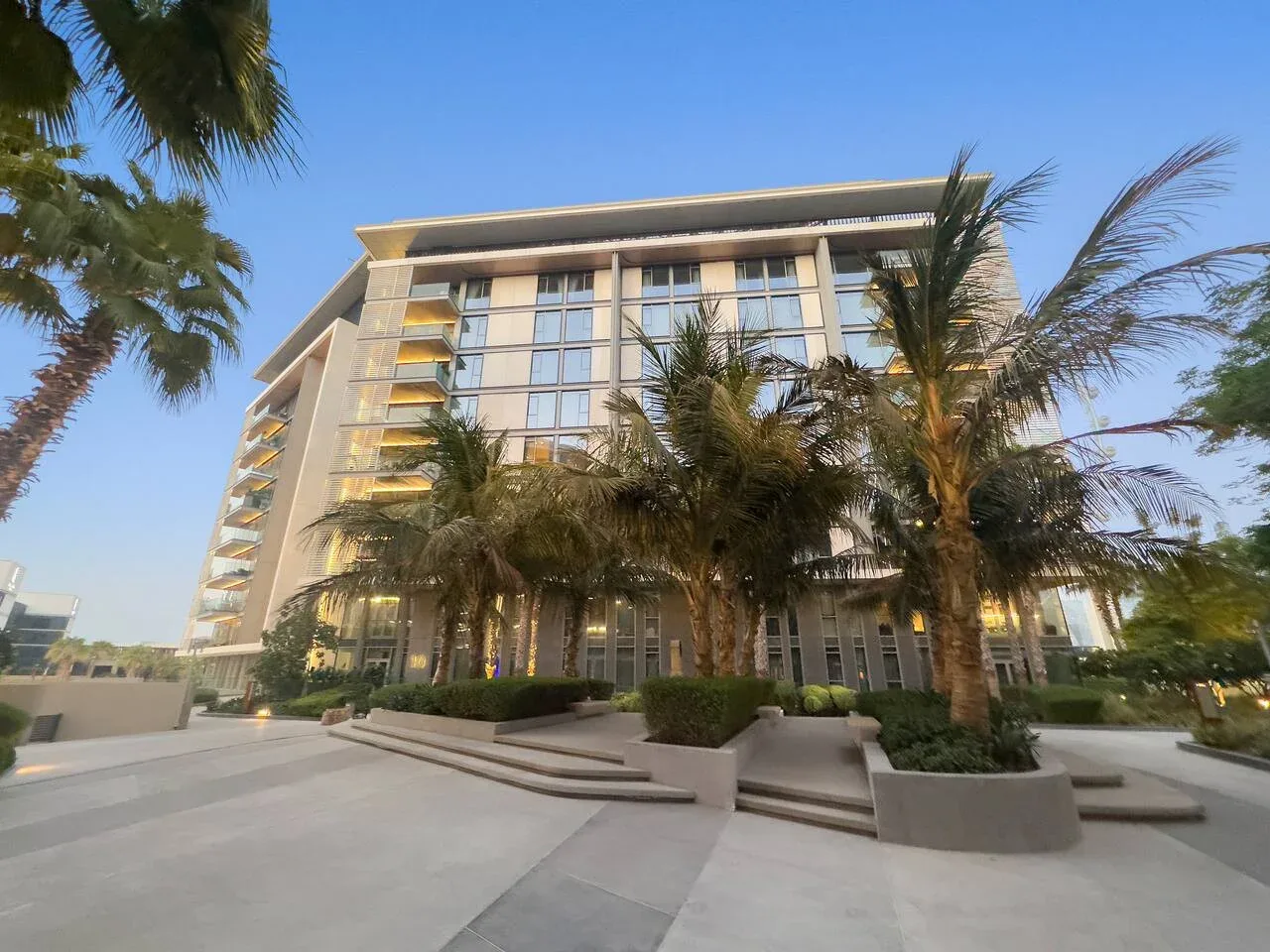 Un edificio moderno se alza tras las palmeras junto a un paseo exterior pavimentado.