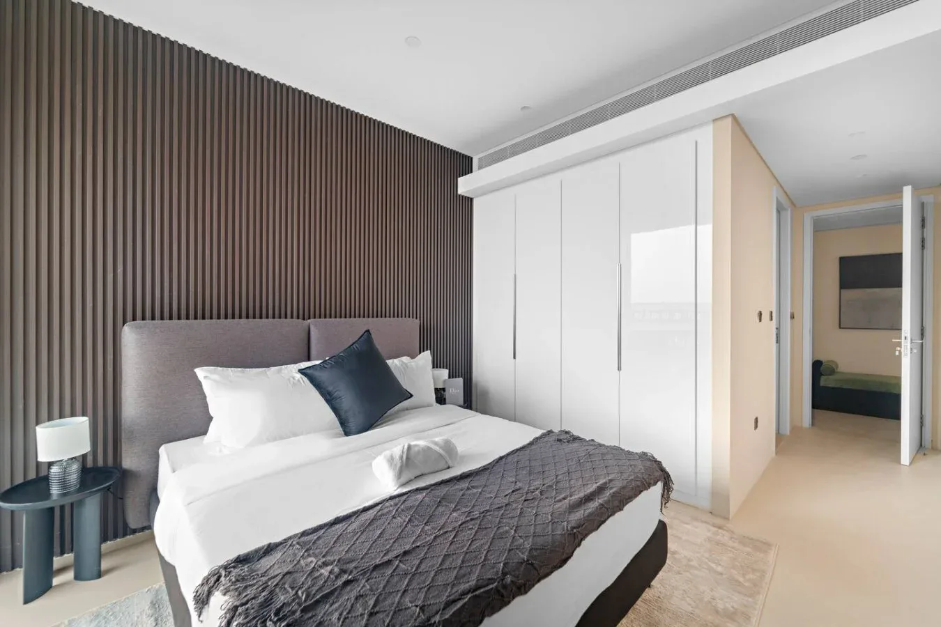 Un dormitorio con una cama vestida con ropa de cama blanca y una manta oscura.